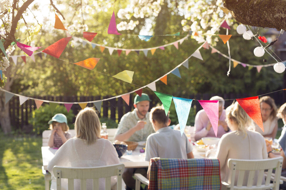 Colourful bunting and paper lanterns strung above a family table at a backyard engagement celebration in evening light